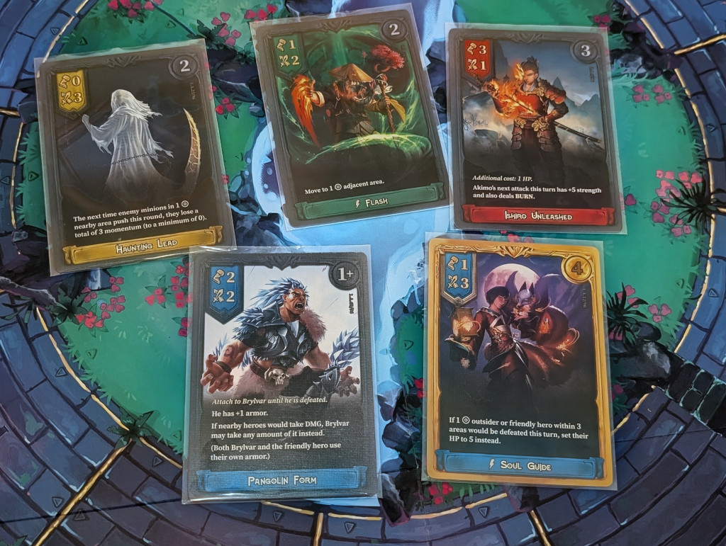 L’esperienza nei giochi di carte da parte dell’editore si vede nella realizzazione di queste carte multiuso: ognuna di esse è utilizzabile per l’assegnazione dei punti all’inizio del turno, può essere pescata per infliggere i danni in alto a destra durante un'azione di attacco e può diventare una spell lanciabile dal personaggio raffigurato se le condizioni lo permettono.